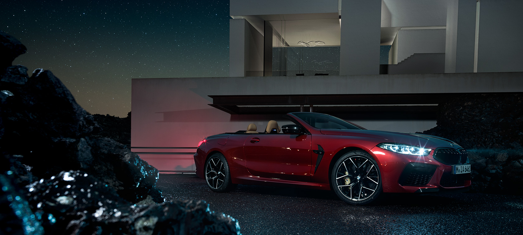 BMW M8 Competition Cabrio in Motegi Red metallizzato, vista laterale di tre quarti, ferma di notte davanti a una villa F91.